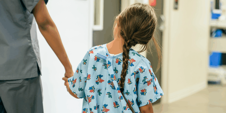 A young girl in a hospital gown with a braid walks hand-in-hand with a healthcare worker down a hallway. (Getty Images)