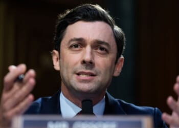 Senator Jon Ossoff appears in a suit and speaks into a microphone, gesturing with his hands during the Senate hearing questioning the Director of National Intelligence nominee Jay Clayton.