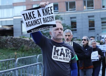 A man protesting racism with RAR stands holding a sign above his head leading a group of protesters outside the an NFL League Meeting on October 17, 2017 in New York City, NY.