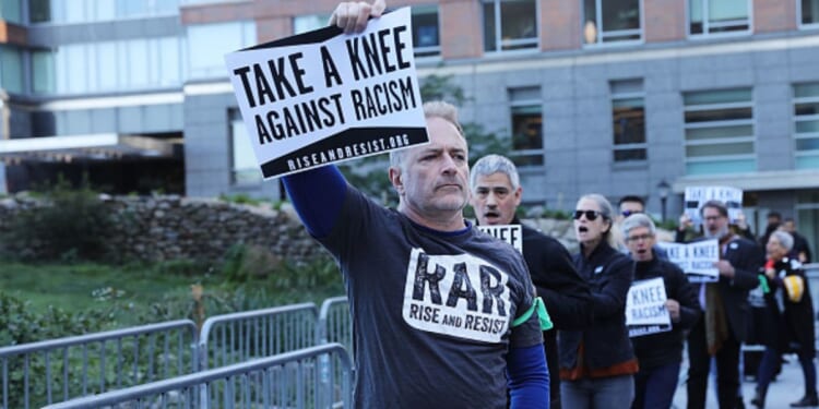 A man protesting racism with RAR stands holding a sign above his head leading a group of protesters outside the an NFL League Meeting on October 17, 2017 in New York City, NY.