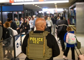 An ICE agent stands alongside a long line of travelers waiting to pass through a TSA Checkpoint at the Philadelphia International Airport on March 28, 2026, in Philadelphia, Pennsylvania.