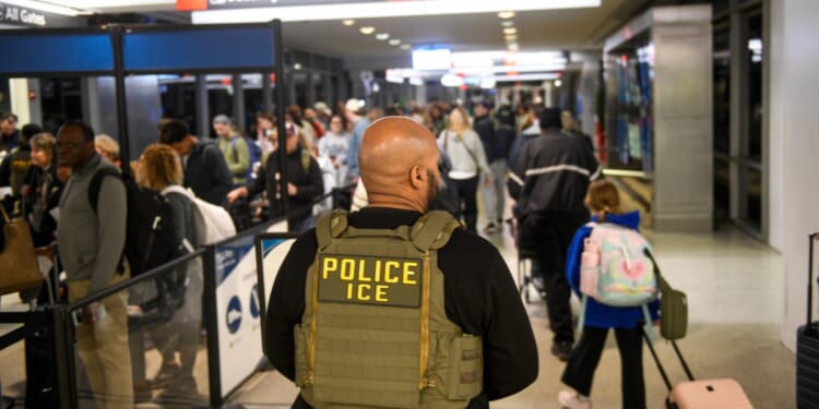 An ICE agent stands alongside a long line of travelers waiting to pass through a TSA Checkpoint at the Philadelphia International Airport on March 28, 2026, in Philadelphia, Pennsylvania.