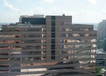 A tall building with the sign Texas Childrens Hospital on the top, surrounded by other office buildings under a partly cloudy sky.