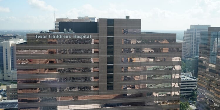 A tall building with the sign Texas Childrens Hospital on the top, surrounded by other office buildings under a partly cloudy sky.