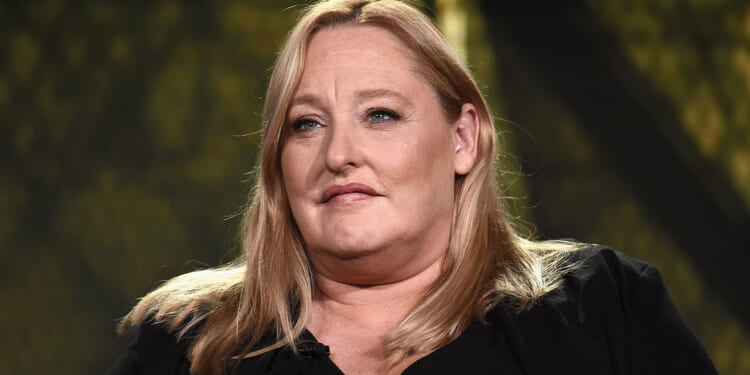 Former SPLC CFO Heidi Beirich, founder of the Global Project Against Hate and Extremism, got arrested Wednesday. Pictured: Beirich, a woman with long blonde hair and a black top sits in front of a blurred background, looking slightly to the side with a neutral expression.