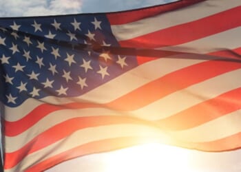 An American flag flies as the sun shines behind it.