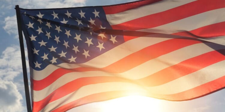 An American flag flies as the sun shines behind it.