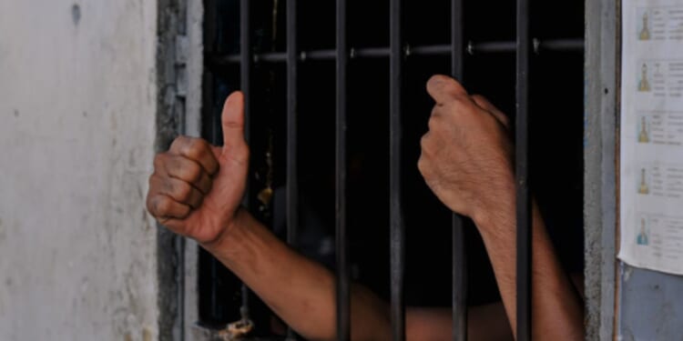 A prisoners hands are reaching from behind cell bars.