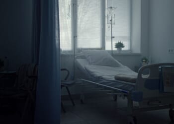 A hospital bed sits empty in a corner.