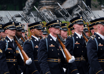 A group of uniformed soldiers marches in formation, carrying rifles with bayonets fixed, during a ceremonial parade.