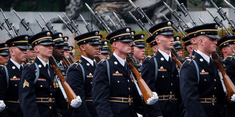 A group of uniformed soldiers marches in formation, carrying rifles with bayonets fixed, during a ceremonial parade.