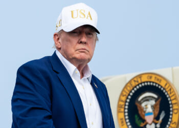 A man in a blue suit and white USA hat stands in front of a partial view of the presidential seal.