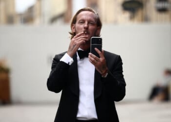 British actor Laurence Fox gestures with his phone, live-streaming, as he stands behind security barriers after arriving to attend a speech by British far-right activist Tommy Robinson to The Oxford Union, in Oxford, western England, on June 17, 2026.
