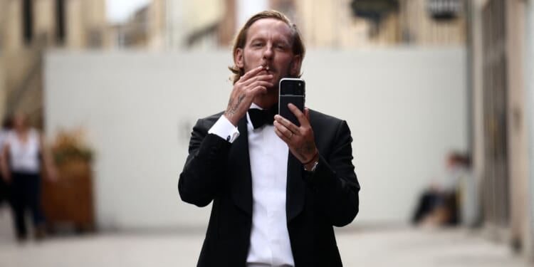 British actor Laurence Fox gestures with his phone, live-streaming, as he stands behind security barriers after arriving to attend a speech by British far-right activist Tommy Robinson to The Oxford Union, in Oxford, western England, on June 17, 2026.