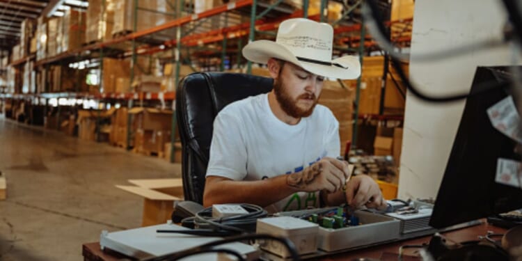 A man wearing a cowboy hat sits at a table and works.