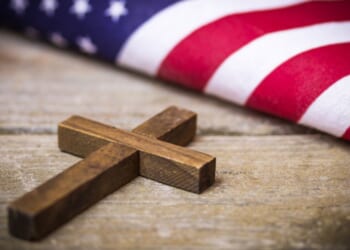 A cross and an American flag sit next to each other on a wooden table.