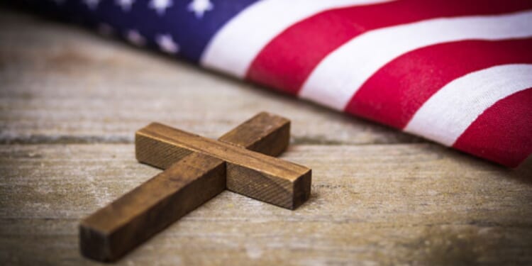 A cross and an American flag sit next to each other on a wooden table.