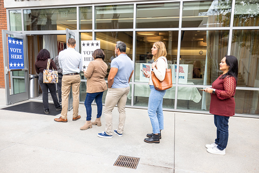 People stand in a line outside a polling center during the day.