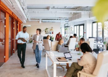Employees work in and walk through a modern-looking workspace.