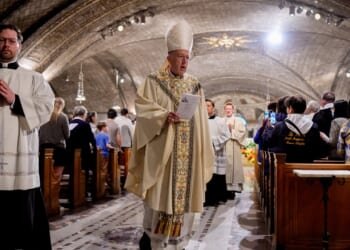 A Catholic bishop and altar server process at the end of Mass in a crowded church