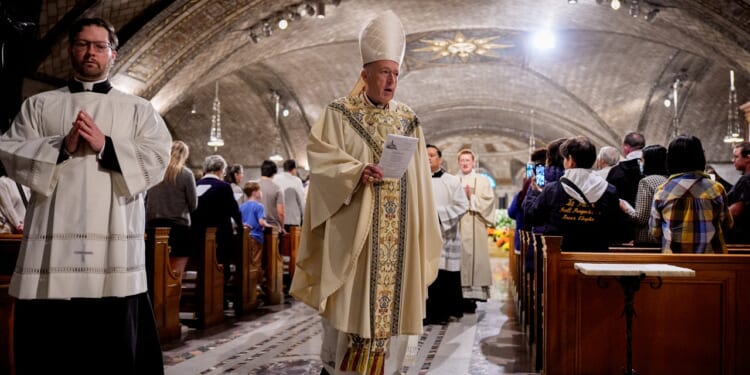A Catholic bishop and altar server process at the end of Mass in a crowded church