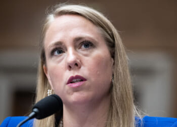 EEOC Chair Andrea R. Lucas has argued for scrapping mandatory racial reporting for employers. The reporting has become a weapon for the DEI movement. Pictured: Lucas, a woman with long blonde hair speaks into a microphone at a formal event, wearing a blue blazer and pearl earrings, with a serious expression.