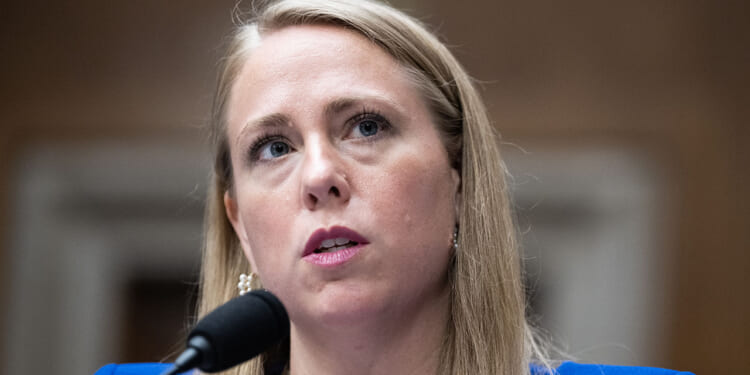 EEOC Chair Andrea R. Lucas has argued for scrapping mandatory racial reporting for employers. The reporting has become a weapon for the DEI movement. Pictured: Lucas, a woman with long blonde hair speaks into a microphone at a formal event, wearing a blue blazer and pearl earrings, with a serious expression.