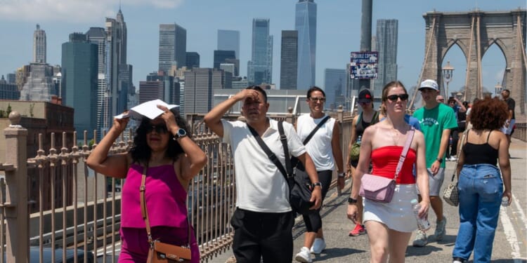 People walk across the Brooklyn Bridge on a day where the heat index is expected to top 100 degrees on July 25, 2025, in the Brooklyn borough of New York City.