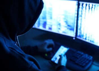 A hacker works on a computer and phone.