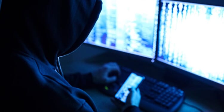 A hacker works on a computer and phone.