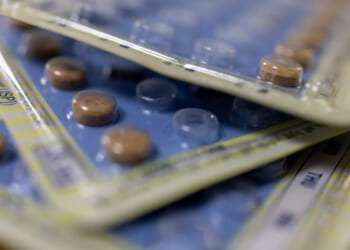 Close-up of several overlapping blister packs with round brown tablets inside, some tablets removed, on a wooden surface.