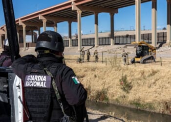 A Mexican National Guard soldier stands on the south side of the border as Texas National Guard troops place posts to extend a secondary fence at the U.S.-Mexico border on Jan. 7, 2023, as viewed from Ciudad Juarez, Mexico.