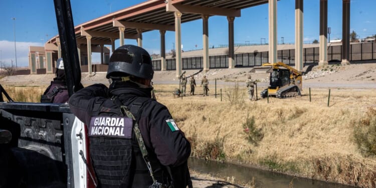 A Mexican National Guard soldier stands on the south side of the border as Texas National Guard troops place posts to extend a secondary fence at the U.S.-Mexico border on Jan. 7, 2023, as viewed from Ciudad Juarez, Mexico.