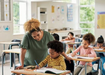 A teacher helps a child in an elementary school classroom.