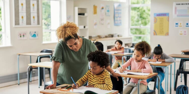 A teacher helps a child in an elementary school classroom.