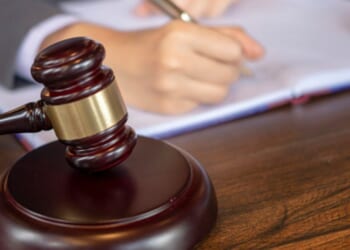 A person writes on a page as a gavel sits next to them.