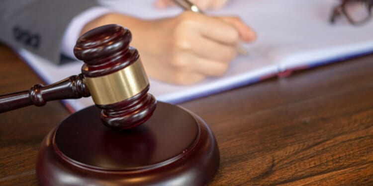 A person writes on a page as a gavel sits next to them.