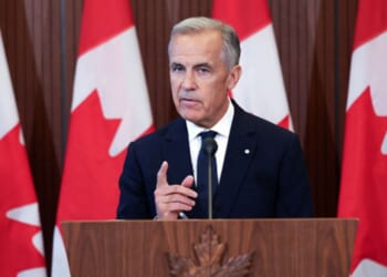 Canadian Prime Minister Mark Carney speaks to the press behind a wooden podium as Canadian flags stand behind him near a wall on September 8, 2026.