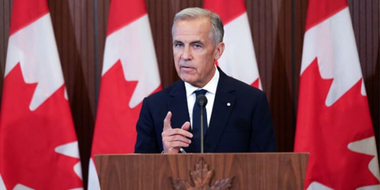 Canadian Prime Minister Mark Carney speaks to the press behind a wooden podium as Canadian flags stand behind him near a wall on September 8, 2026.