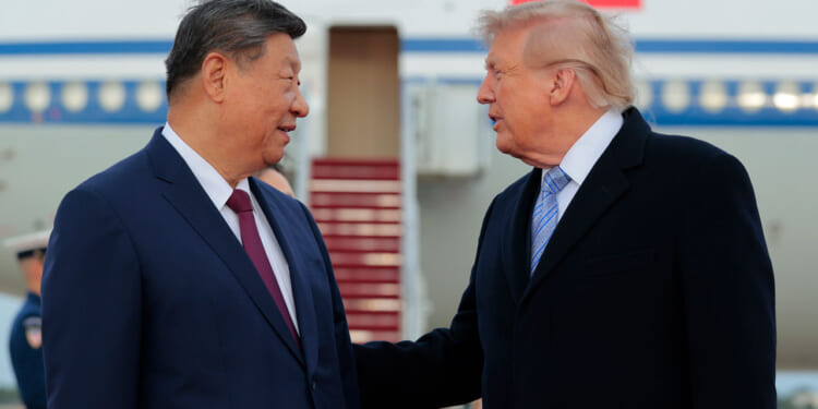 Xi Jinping and Donald Trump in suits stand outdoors, talking to each other. Xi faces forward, smiling, while Trump gestures with his hand. An airplane with a staircase is visible in the background.