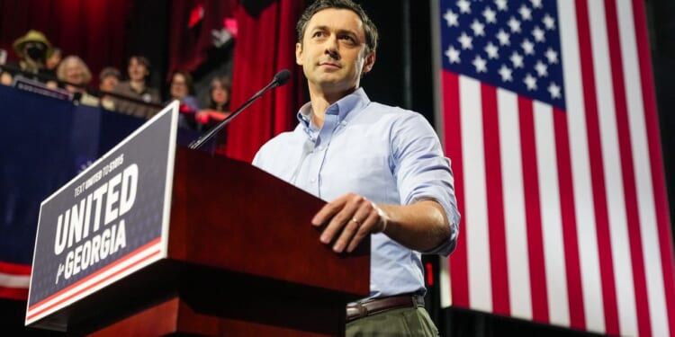 Sen. Jon Ossoff stands at a podium labeled UNITED FOR GEORGIA with an American flag in the background and people watching from the side.