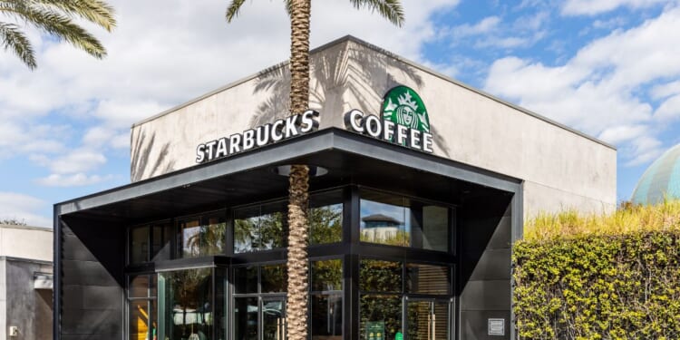 A modern Starbucks Coffee building with a palm trees and a blue sky.
