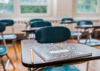 A notebook and pencil on a desk in a school classroom.