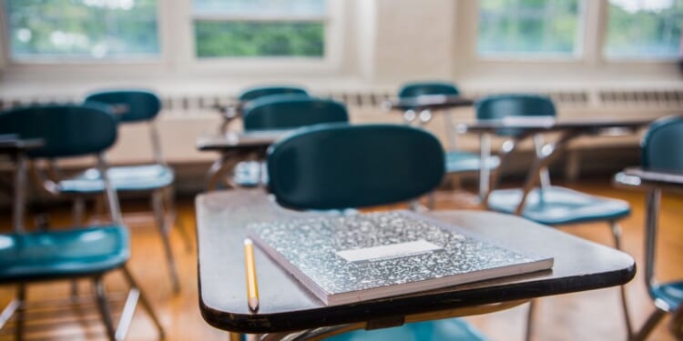 A notebook and pencil on a desk in a school classroom.