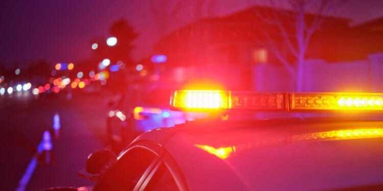 A police car at night alongside a road with emergency lights flashing.