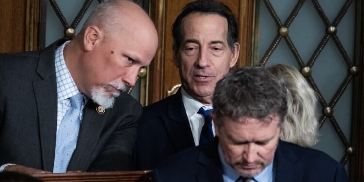 Three men in suits are gathered closely together, appearing to have a serious discussion. Two men are standing, one is leaning in to speak, while the third man sits in front of them, looking down. Ornate wooden doors are in the background.