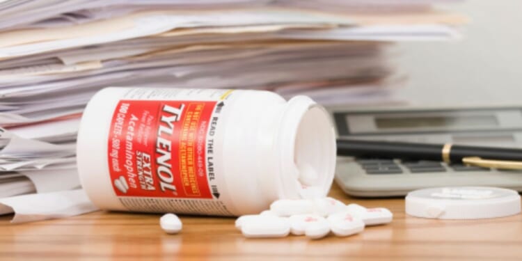 A Tylenol bottle is flipped over with pills pouring out.