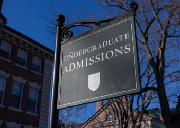 A black sign reads Undergraduate Admissions outside a brick building, with bare tree branches and a clear blue sky in the background.