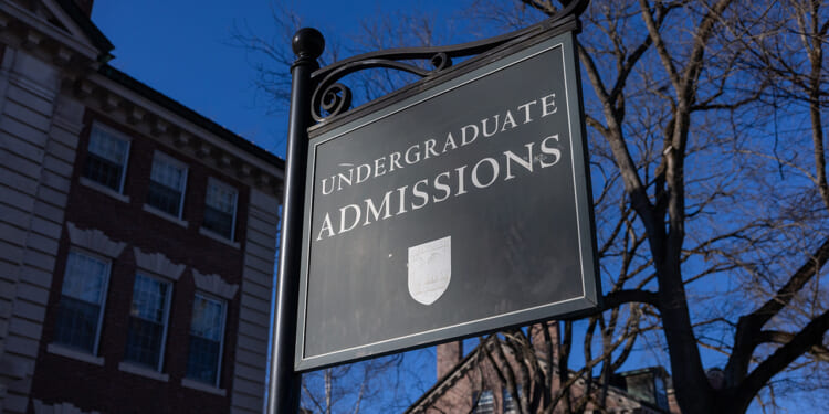 A black sign reads Undergraduate Admissions outside a brick building, with bare tree branches and a clear blue sky in the background.