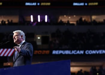 Rep. Mike Collins is pictured in a suit and speaks at a podium during the Republican National Convention, with REPUBLICAN CONVENTION and 2028 visible on a screen in the background, and an audience in a darkened arena.